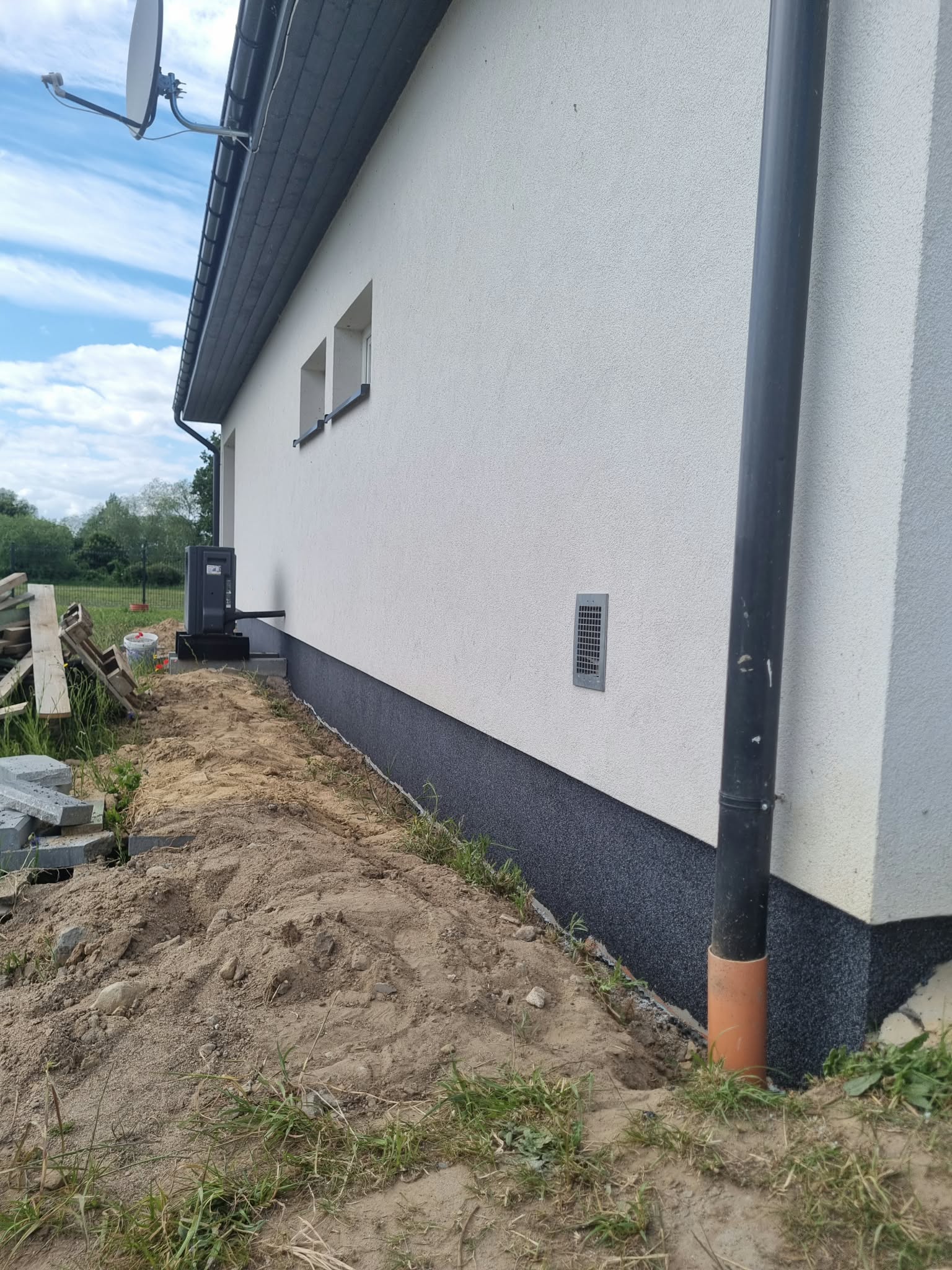 Ciemna warstwa wykończeniowa cokołu zestawiona z jasną elewacją. Prace przy otoczeniu budynku nadal trwają.