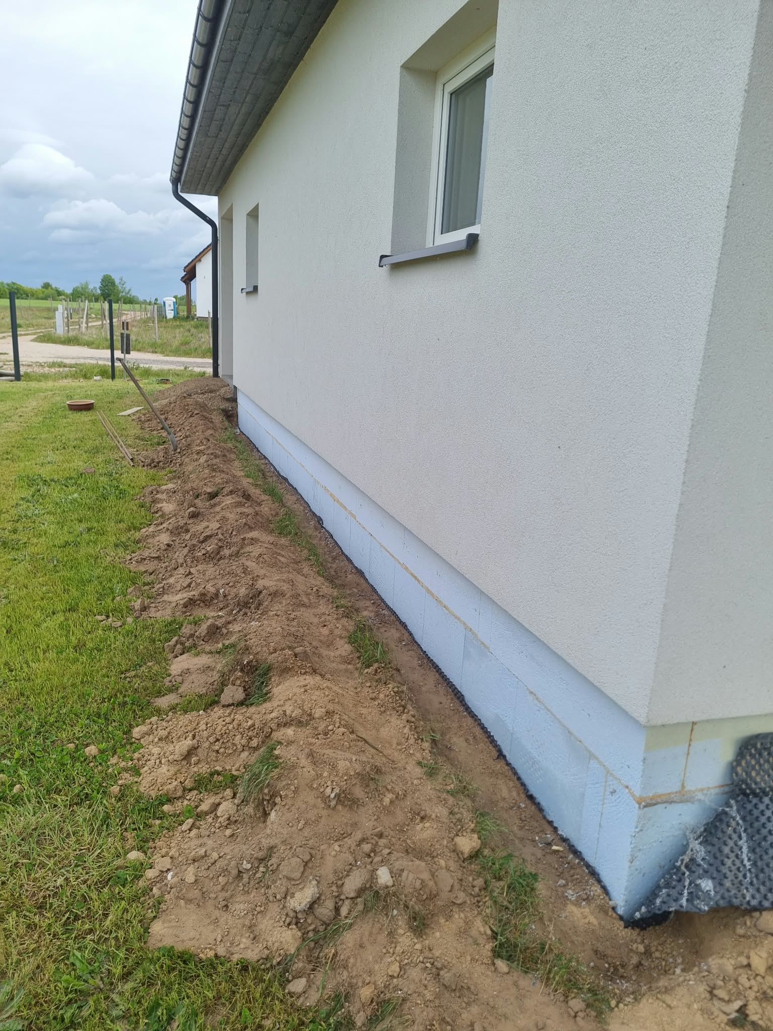 Widok jasnej elewacji, parapetów oraz narożnika z niewykończonym jeszcze cokołem.